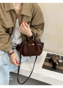 Retro brown suede shoulder bag featuring a chic metal clasp, top handle, and plush pom-pom charm.