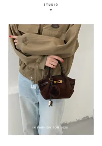 Brown suede handbag detail showcasing metal clasp closure, top handles and chic furry pompom.