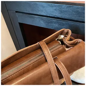 Dettaglio borsa a tracolla in pelle marrone, consistenza premium, cerniera metallica e cuciture.