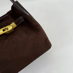 Detail view of dark brown suede handbag with golden metal turn-lock closure and leather trim.