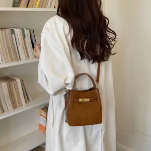 Detailed view of brown suede bucket bag with gold lock closure and shoulder strap detail.