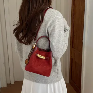 Wine red suede bucket bag detail, featuring gold turn-lock closure and cute charm pendant.