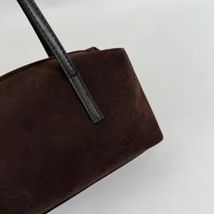 Vue détaillée du sac bandoulière en daim marron avec poignée en cuir noir texture.