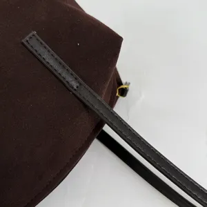 Gros plan détail du sac porté épaule en suédine marron foncé avec fine lanière en cuir.