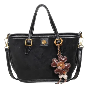 Black suede tote bag with top handles, shoulder strap, and cute flower charm accent.