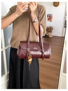 Detail view of dark red oil wax leather baguette bag, featuring slim straps and beaded charms.