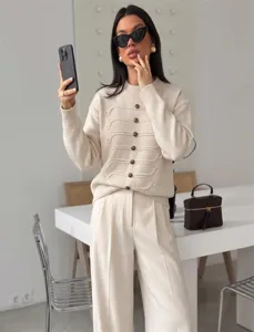 Detailaufnahme eines schicken, beige Pullovers mit Knöpfen, getragen im hellen Raum.