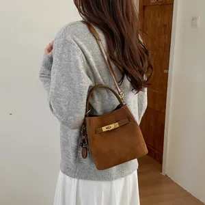 Brown suede bucket bag detail featuring metal turn-lock closure and shoulder strap design.