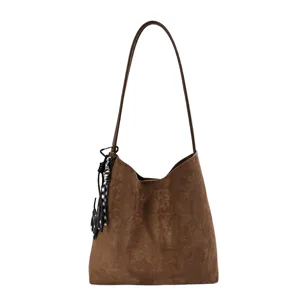 Close-up detail of the brown suede shoulder bag featuring a chic hanging charm and strap.