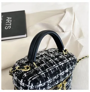 Gedetailleerde opname van de luxe zwart-witte tweed vanity tas met gouden ketting.