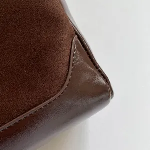 Brown shoulder bag detail view, suede and glossy leather contrast stitching design.