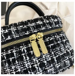 Detail van de stijlvolle zwart-witte tweed vanity tas met gouden ritsen en handvat.