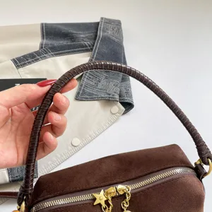 Brown suede handbag detail, featuring a unique braided handle and gold star zipper pulls.