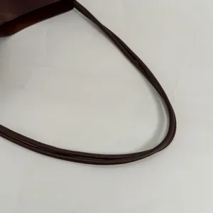 Detailed shot of dark brown suede handbag double shoulder strap with neat edge stitching.
