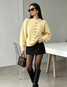 Nahaufnahme eines eleganten gelben Strickpullovers mit geflochtenen Knöpfen und langen Ärmeln.