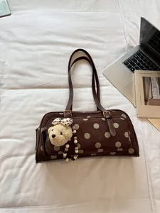 Sac à bandoulière à pois marron en détail, pendentif d'ours sur fond de tissu blanc.