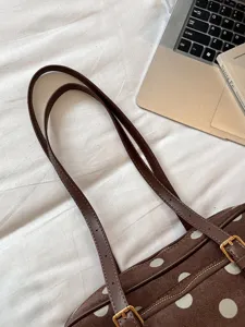 Détail de sac à épaule marron à pois, texture daim vintage avec doubles lanières et boucles métal.
