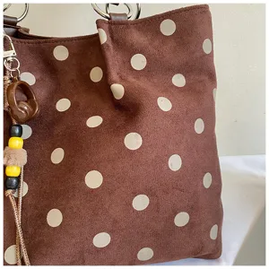 Close-up detail shot of brown suede polka dot tote bag showing texture and handle hardware.