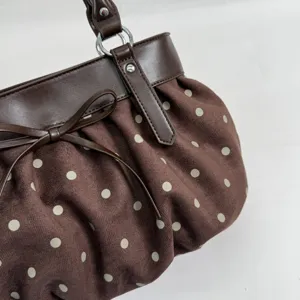 Close-up detail of brown polka dot shoulder bag with cute bow and gathered fabric design.