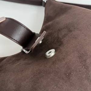 Close-up view of brown suede handbag hardware, magnetic snap closure and strap detail.