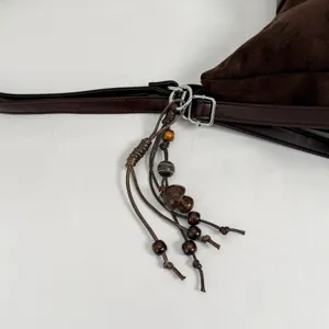 Brown suede shoulder bag detail showcasing decorative beaded tassel and metal hardware.