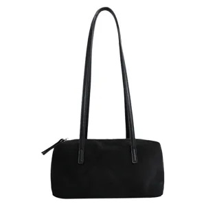 Close-up of black suede pillow shoulder bag, minimalist cylindrical design with long straps.