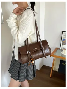 Detailed view of brown oil-wax leather baguette shoulder bag with chic buckle and bead tassel.