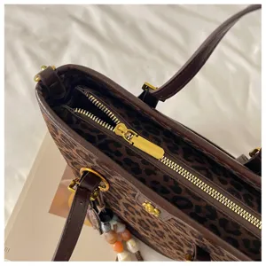 Stylish leopard print tote bag with brown leather trim, gold zipper, and elegant charm detail.
