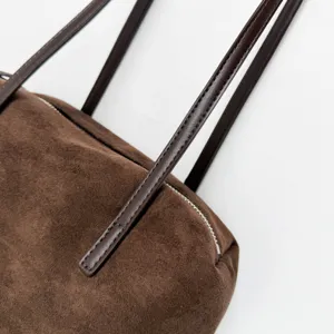Brown suede shoulder bag detail showcasing soft texture, dark leather strap and metal zipper.