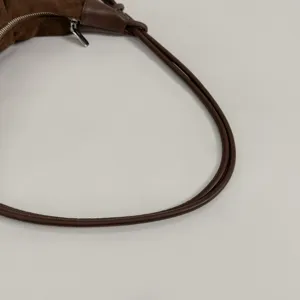 Detailaufnahme des braunen Wildleder Umhängetaschenriemens mit glattem Leder und Metallreißverschluss.