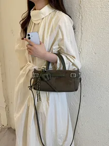 Détail de sac à main en suède vert foncé avec boucle métallique et bandoulière réglable.