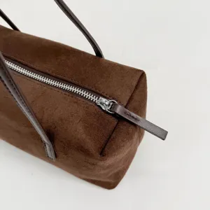 Brown suede pillow bag detail showing the smooth silver zipper, thin straps, and soft texture.