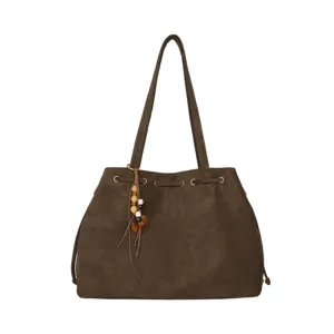 Nahaufnahme der dunkelbraunen Wildleder-Schultertasche mit Metallösen und Perlenanhänger.