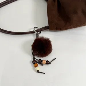 Brown suede shoulder bag detail showing fuzzy pom-pom and wooden bead charm accessory.