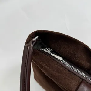 Brown suede shoulder bag detail close-up, showing metallic zipper and premium texture.