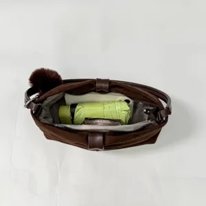 Brown suede shoulder bag detail showing interior capacity with chic fluffy pom-pom charm accessory.