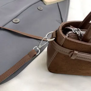 Brown suede and leather handbag detail showing silver hardware, zipper, and shoulder strap.