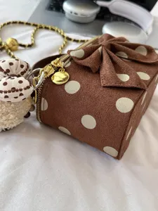 Detail close-up shot of brown polka dot suede box bag with bow and gold chain.
