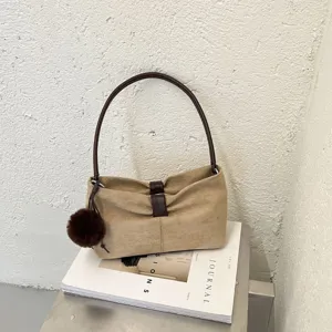 Minimalist suede shoulder bag for women, chic brown handbag with fluffy pom-pom charm and top handle.