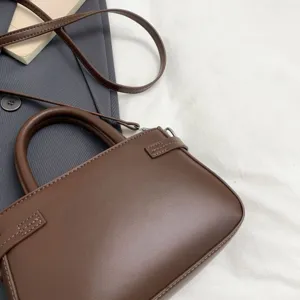 Close-up detail of the brown leather handbag, showing exquisite stitching and texture.