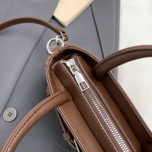 Brown leather handbag detail view, showing exquisite metal zipper and sturdy dual top handles.