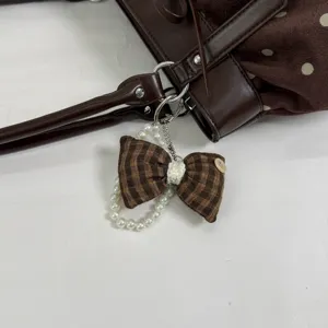 Brown polka dot shoulder bag detail featuring a cute plaid bow and elegant faux pearl keychain.