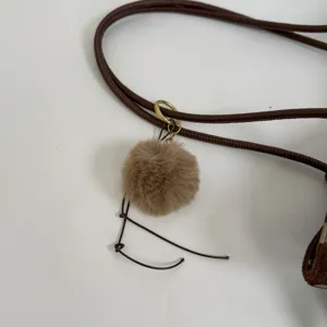 Brown furry pom-pom bag charm detail, stylish handbag accessory and strap close-up view.