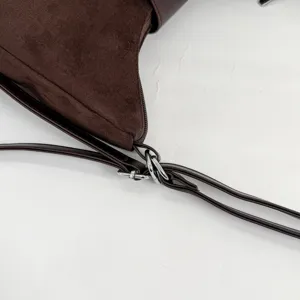 Close-up detail of dark brown suede shoulder bag strap, metal hardware and soft texture.