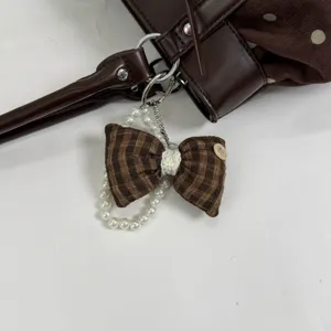 Detailed close-up view of brown plaid bow bag charm with elegant pearl chain accessory.