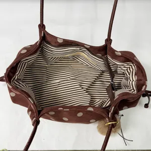 Detailed view of the brown polka dot tote bag interior with striped lining and fluffy charm.