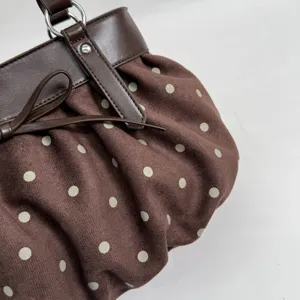 Close-up detail of brown polka dot handbag with bow decoration, soft fabric and leather trim.