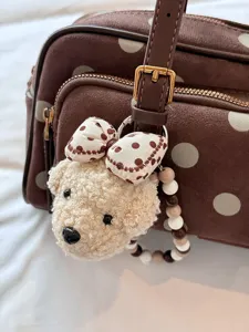 Gros plan détaillé du sac à pois marron avec pendentif ours en peluche et lanière de perles.