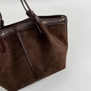 Close-up detail of retro brown suede tote bag, featuring smooth leather handles and pleats.