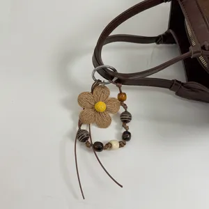 Detailed view of a brown leather tote bag handle with a woven flower and wooden bead charm.